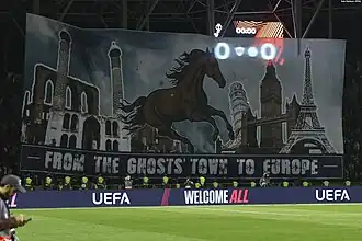 Très grand drapeau montrant un cheval qui galope vers des monuments européens avec le message "From the ghost's town to Europe"