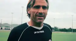 Photographie d'un homme blond, aux cheveux mi-court, avec un t-shirt noir de marque Patrick.