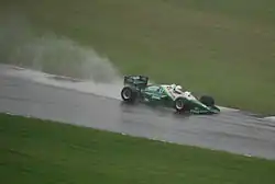 Photo d'une monoplace verte et blanche sur une piste détrempée