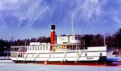 Un bateau blanc de taille moyenne avec une grande cheminée, sur un plan d'eau gelé.