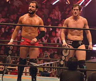 Deux catcheurs avec des ceintures argentées dans les mains.