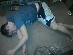 Photo d'un jeune homme inconscient, gisant au sol en position latérale de sécurité, à l'intérieur d'un appartement.