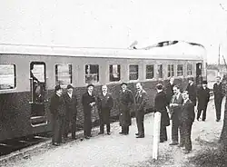 Photographie en noir et blanc d'un autorail à quai devant lequel pose un groupe d'hommes.