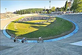 Photographie d'un vélodrome en plein air avec quatre coureurs en piste.