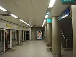 Image d'un quai de la station République avec à gauche les portes palières et à droite un escalier, avec au fond un panneau publicitaire.