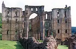 Photographie montrant les ruines d'une vaste église gothique, dont les pierres changent de couleur au-dessus du deuxième niveau d'arcade.