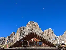 Le Sassolungo derrière le gable du refuge Friedrich August et quelques parapentistes au-dessus.