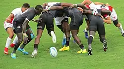 Joueur s'apprêtant à ramasser le ballon derrière une mélée de 2 x 3 joueurs.