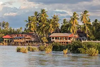 Berge de l'île de Don Khon avec des maisons en bois sur pilotis, au soleil à l'heure dorée, vue depuis Don Det.