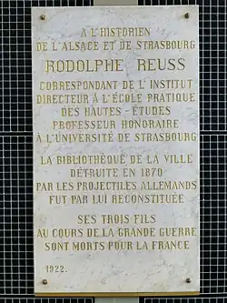 Plaque d'hommage de 1922 : « La bibliothèque de la ville détruite en 1870 par les projectiles allemands fut par lui reconstituée. Ses trois fils au cours de la Grande Guerre sont morts pour la France ».