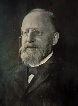 portrait photographique, en noir et blanc, d'un homme d'une soixantaine d'années, au front dégarni, portant un binocle et une barbe claire.