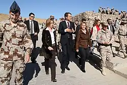 Groupe d'hommes et de femmes en tenues civile ou militaire dans une zone désertique.