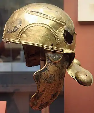 Casque antique doré sur support, de profil, en musée.