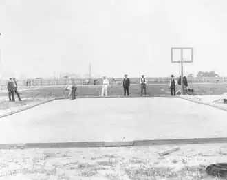 Photographie en noir et blanc d'un terrain couvert de sable entourés par des sportifs et des juges