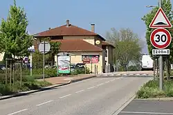 Une route avec deux panneaux à droite dont un indique que la voie est limitée à 30&nbsp;km/h. L'autre panneau indique la présence d'un ralentisseur. À gauche de la route se trouve un abri-bus devant un bâtiment jaune faisant office de restaurant.