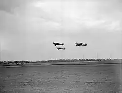 Photographie noir et blanc de trois avions décollant d'un terrain d'aviation.
