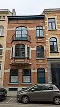 Au no&nbsp;12 : maison de style éclectique teinté d'Art Déco, de trois niveaux de composition asymétrique, construite pour et par les entreprises Caron et Vandiest, 1924. Façade de briques rouges, rehaussée d'éléments enduits en simili-pierre blanche.