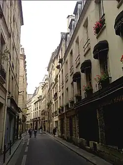 Une rue parisienne étroite avec des immeubles de deux à quatre étages.