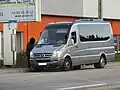 Photographie en couleurs d’un minicar gris en stationnement près d'un bâtiment commercial.