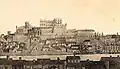 Gravure noire et blanche avec maisons au premier plan, fleuve puis une ville fortifiée en hauteur.