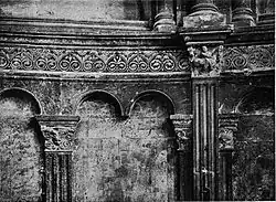 Photographie en noir et blanc montrant les arcatures aveugles du fond de l'abside, surmontées d'une frise décorative.