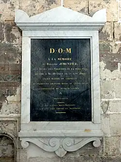 Plaque noire, entourée d'une pierre blanche, accrochée au mur.