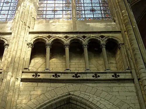 Entre un arc brisé et deux fenêtres vitrées, une galerie ouverte par des arcades composées de 5 lancettes séparées par des colonnettes.