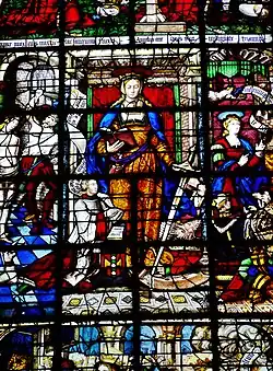 Élément de vitrail. Au centre de l'image, une femme habillée en orange porte une épée et un livre rouge. Des hommes sont agenouillés à ses pieds. À gauche, un homme barbu torse nu frappe à coups de verge une femme. Des phylactères sont visibles.