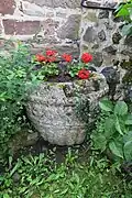 Baptistère roman, servant de jardinière, accolé au mur nord à droite du portail.
