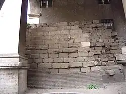 Photographie en couleurs d'un mur en moellons réguliers sous une arche maçonnée.