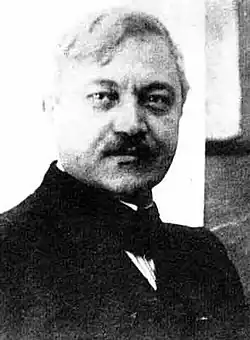  Image en noir et blanc d'un buste d'homme position trois quart, visage jovial avec moustache.