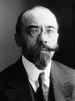 Photographie d'un homme blanc d'une quarantaine d'années, le front dégarni, des lorgnons sur le nez, portant des moustaches et une barbiche