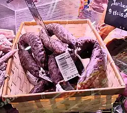 au moins quatre saucisses de foie dans un panier rectangulaire dans une vitrine réfrigérée, les saucissons sont étiquetés