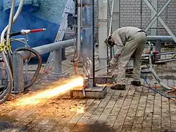 Un homme découpe au chalumeau un pilier métallique à sa base.