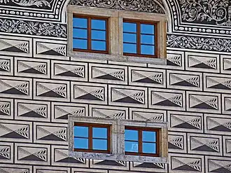 Vue des sgraffites en forme de bossages d'une façade, percée de quatre petites fenêtre à carreaux.