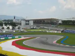Piste goudronnée de Formule 1 au niveau d'une chicane, avec une tribune en arrière plan