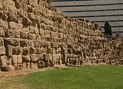 Photographie en couleurs d'un mur fait de gros blocs dont la surface est irrégulière.