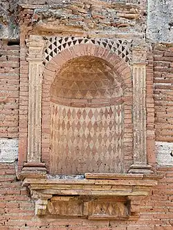 Vue d'une niche dans un mur, décorée de motifs géométriques et brique rouge et pierre blanche.