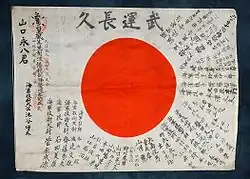 Petite pièce de tissu sur laquelle il y a un drapeau japonais entouré de phrases porte-bonheur.