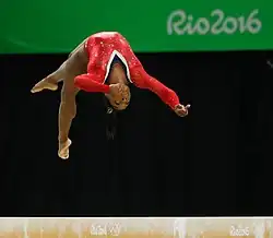 Photo de Simone Biles en justaucorps rouge, la tête en bas pendant un saut sur la poutre.