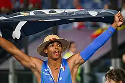 Photo de Lorenzo Simonelli, maillot bleu de l'Italie entrouvert sur la poitrine, brandissant un drapeau One Piece.