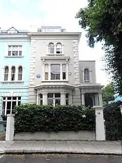 Photographie centrée sur la façade d'un bâtiment. Au premier étage, à côté d'une fenêtre, est fixée un disque bleu sur lequel est écrit un texte sur Osbert Lancaster.