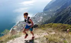 photographie d'un sportif courant sur les hauteurs montagneuse avec en arrière fond une ville au bord de l'eau