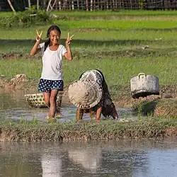 Une jeune Laotienne dans une rizière faisant un signe V de chaque main (2018)