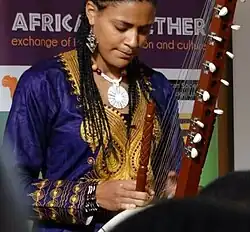 Une femme à la peau brune et claire, portant de fines nattes africaines lui tombant sur les épaules, joue en fermant les yeux de la kora. Derrière, on peut lire sur une affiche "Africa Together".