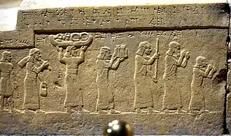 Bas-relief du podium du trône assyrien du palais du Fort Salmanazar de Nimroud, face sud : le roi Salmanazar&nbsp;III reçoit le tribut de Chaldéens, comprenant de l'étain, du bois précieux et de l'ivoire. Musée national d'Irak.
