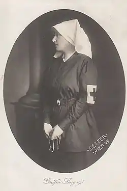 Photographie en noir et blanc, sertie dans un cadre ovale, montrant Stéphanie de profil, coiffée d'une voilette blanche, brassard de la croix-rouge au bras gauche et tenant un chapelet entre les mains.