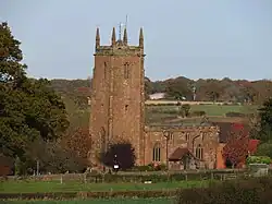 Photo d'un bâtiment en pierre rouge flanqué d'une grande tour carrée. Il se dresse au cœur d'un paysage verdoyant