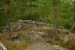 Tas de pierres indiquant un ancien mûr sur une colline rocheuse et boisée.