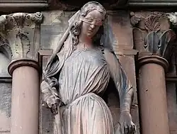 Tête aux yeux bandés et buste féminin sculptés, avec de chaque côté des colonnes de grès rose.